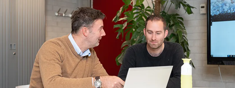 Twee collega's kijken naar een post-it op een raam.
